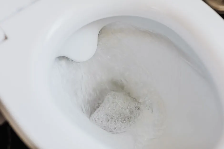 High angle of clean white ceramic toilet bowl with flushing foamy water in bathroom